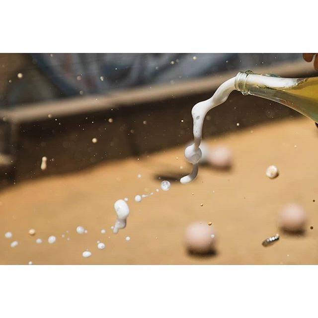 Beer being poured from a glass bottle, creating foam against a tan background.