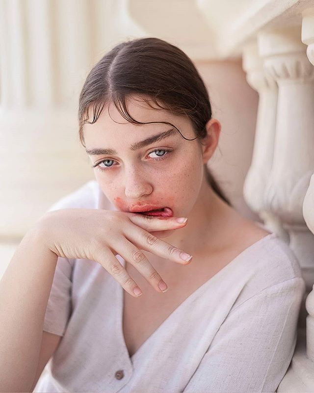 Intense portrait of a young woman with smudged lipstick leaning against a white pillar.