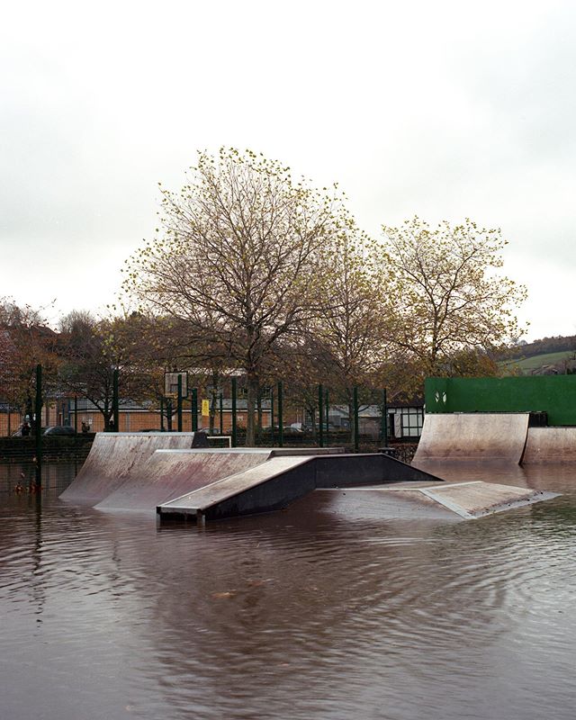 A flooded skatepark showing submerged ramps and trees in the background due to heavy rainfall.