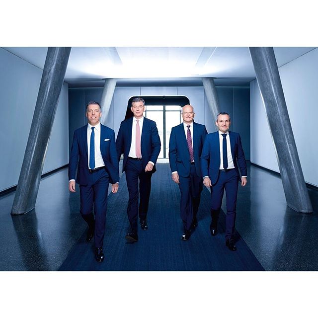 Four businessmen in suits walk confidently down a modern office corridor, symbolizing leadership and corporate strategy.