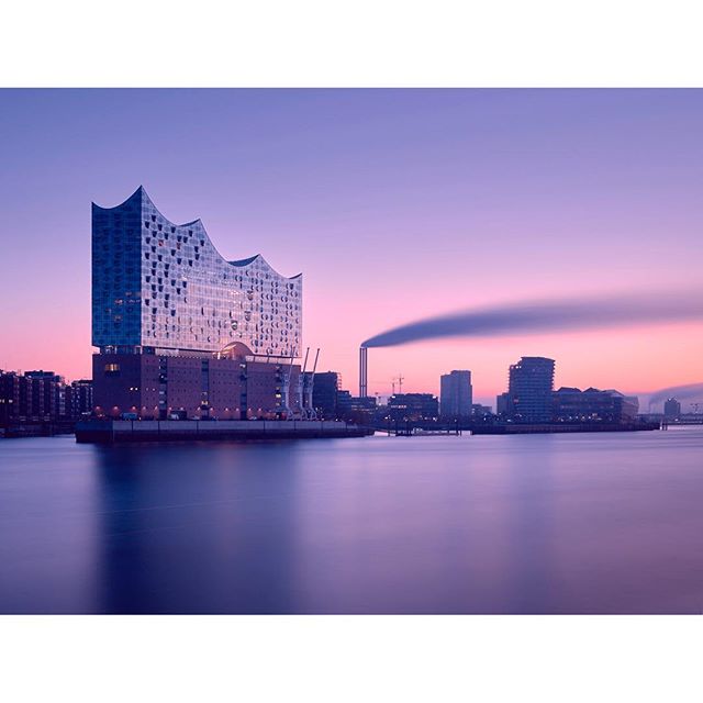 The Elbe Philharmonic Hall in Hamburg stands tall amidst a serene cityscape during a peaceful, colorful sunset.